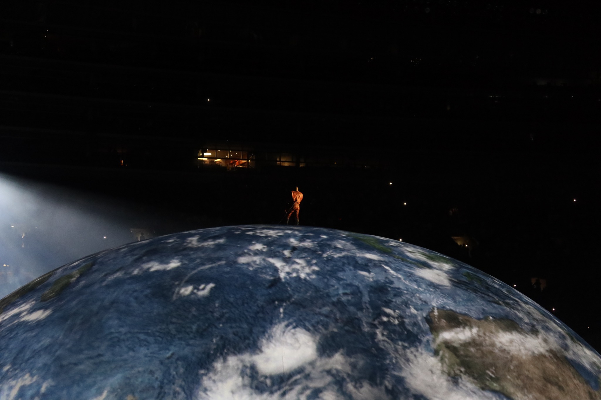 A distant performer standing atop the globe